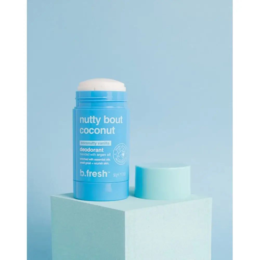 Deodorante blu con coperchio bianco. Scritta: "nutty bout coconut". Accanto il coperchio. Su un piedistallo blu.