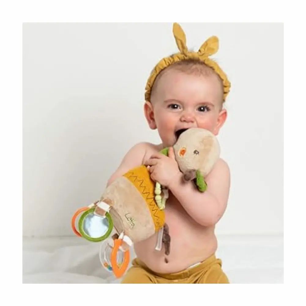 Bambino morde una giraffa di peluche. Beige, verde e giallo. Anelli e specchi. Scritta "Lotta". Il bambino indossa una fascia.