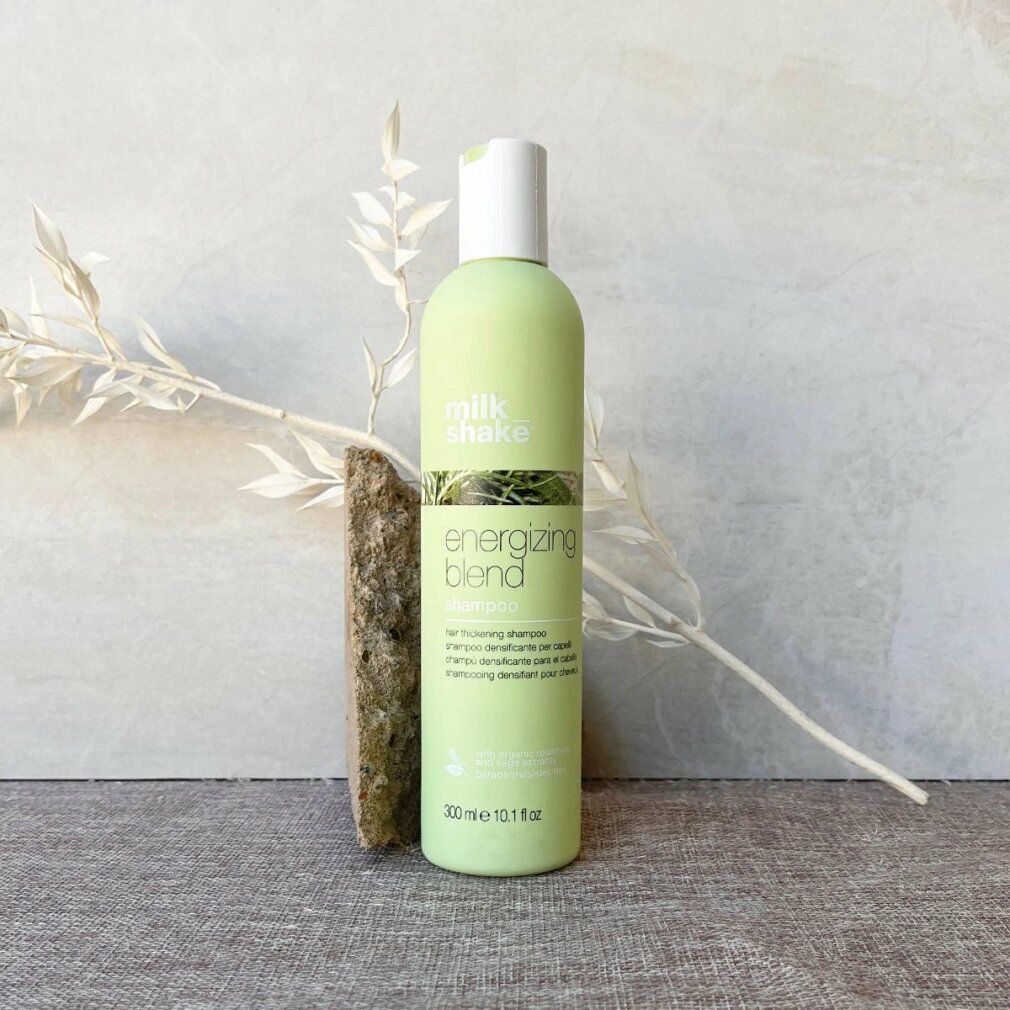 Flacone di shampoo verde chiaro con tappo bianco. Scritta: energizing blend shampoo. Vicino a pietra e ramo.