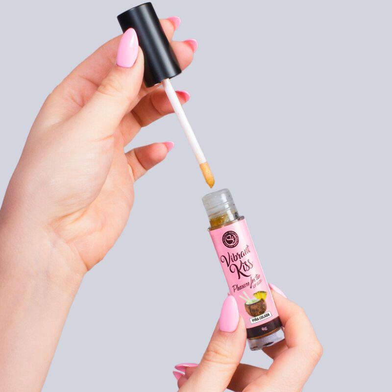 Flacone di lucidalabbra con applicatore, tenuto da due mani. Scritta: Vibrant Kiss, Pina Colada.