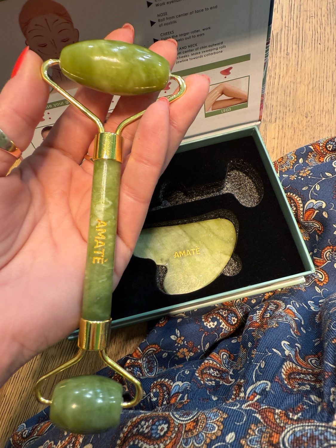 Rullo e pietra Gua Sha in giada in confezione aperta. Confezione con istruzioni. Mano che tiene il rullo.