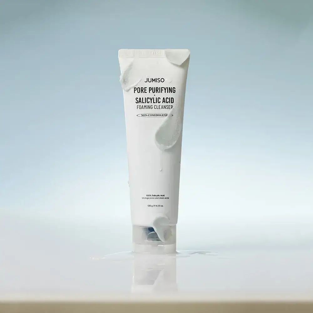 Tubo bianco con prodotto. Scritta: JUMISO Pore Purifying Salicylic Acid Foaming Cleanser. 150 g / 5.27 oz. Su sfondo blu.