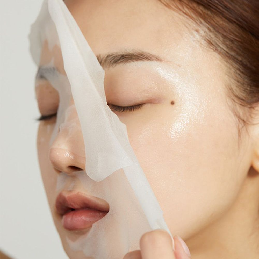 Viso di persona con maschera in tessuto bianco parzialmente rimossa. La pelle è lucida.