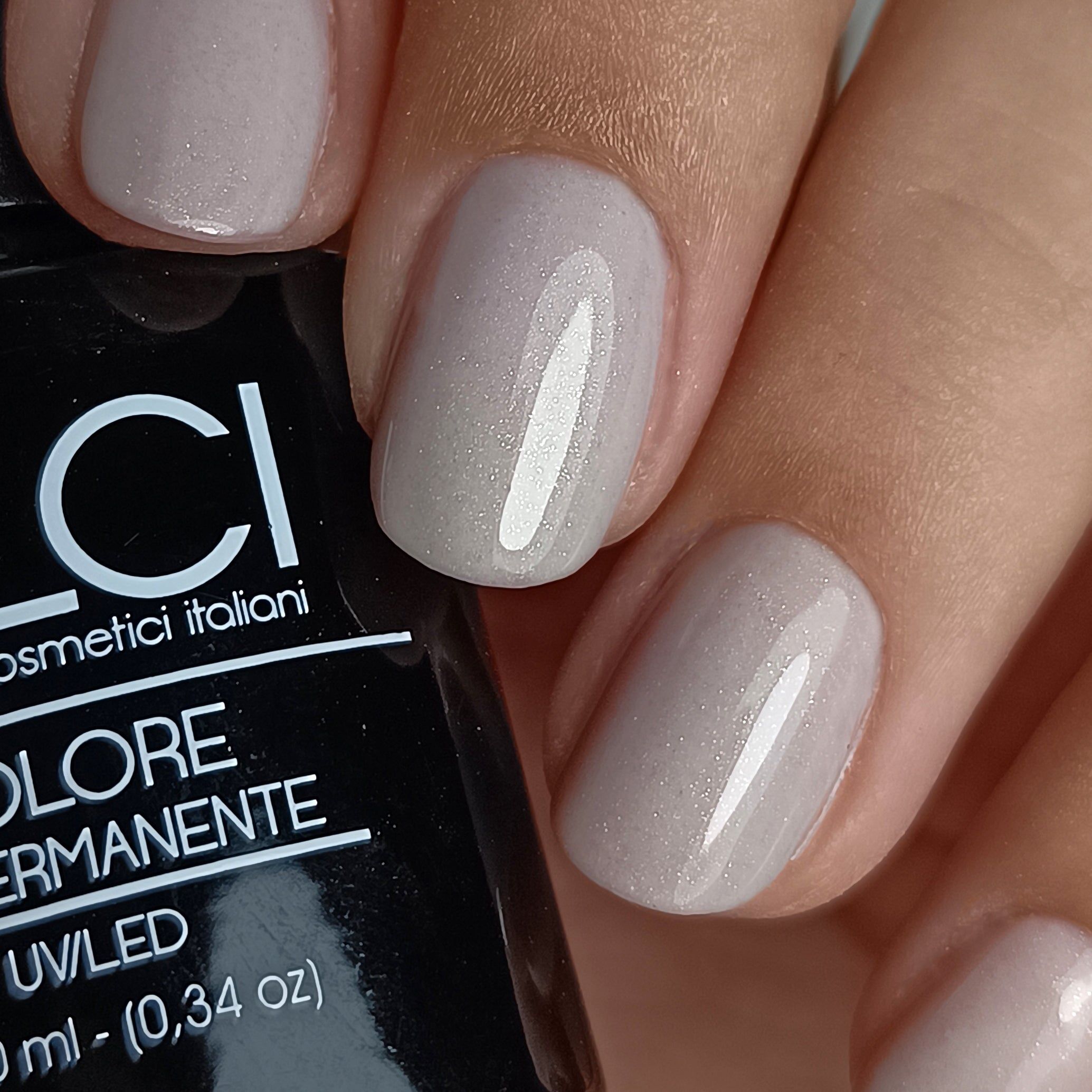 Primo piano di unghie smaltate e flacone di smalto. Unghie smaltate di grigio. Flacone con logo e testo.