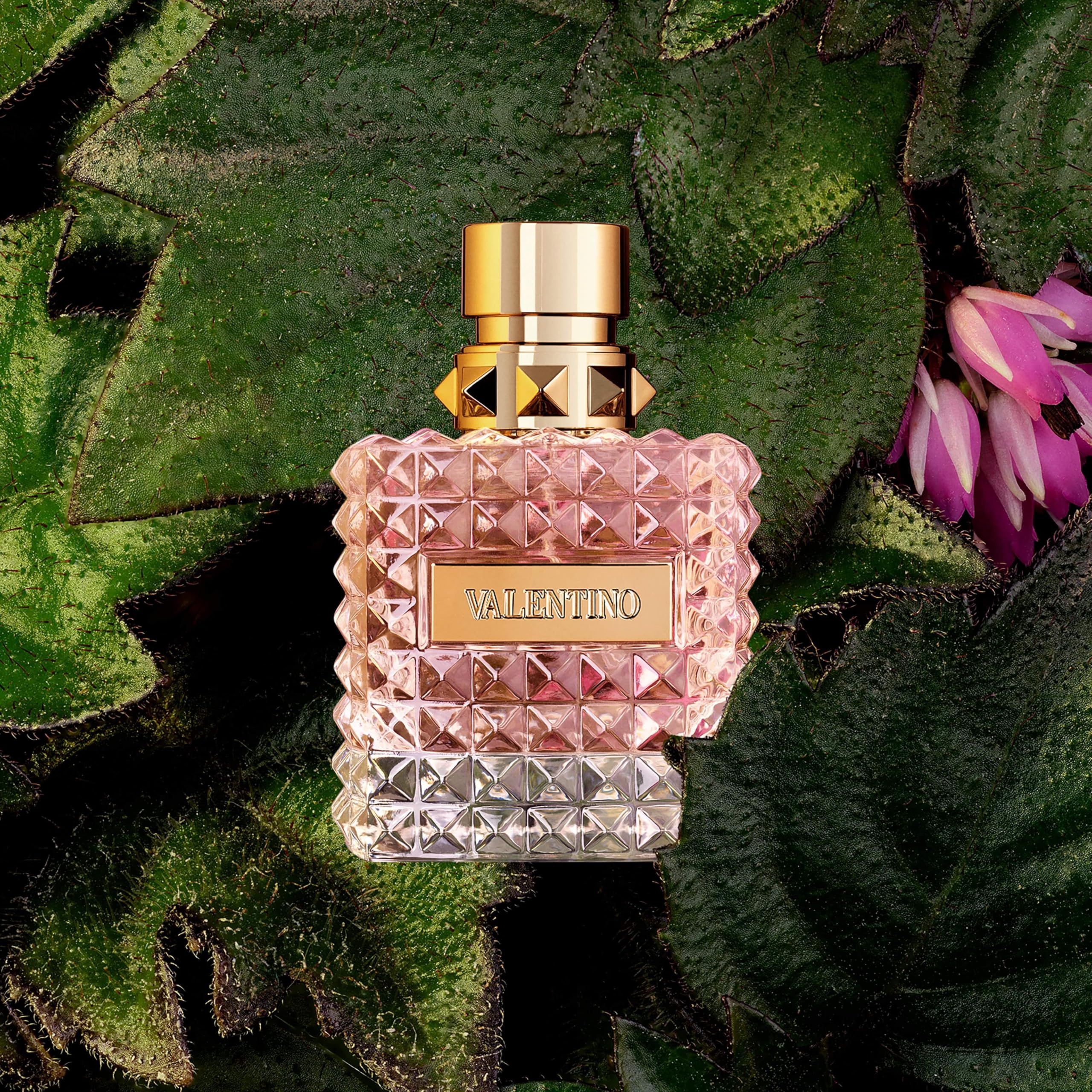 Flacone di profumo su foglie. Tappo dorato, vetro sfaccettato quadrato. Scritta: VALENTINO.