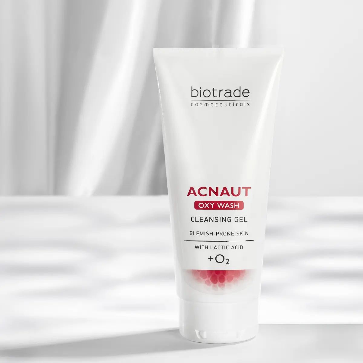 Tubo bianco con testo rosso e nero. ACNAUT OXY WASH CLEANSING GEL. Per pelli a tendenza acneica. Con acido lattico + O2. Marchio: Biotrade. Sfondo bianco.