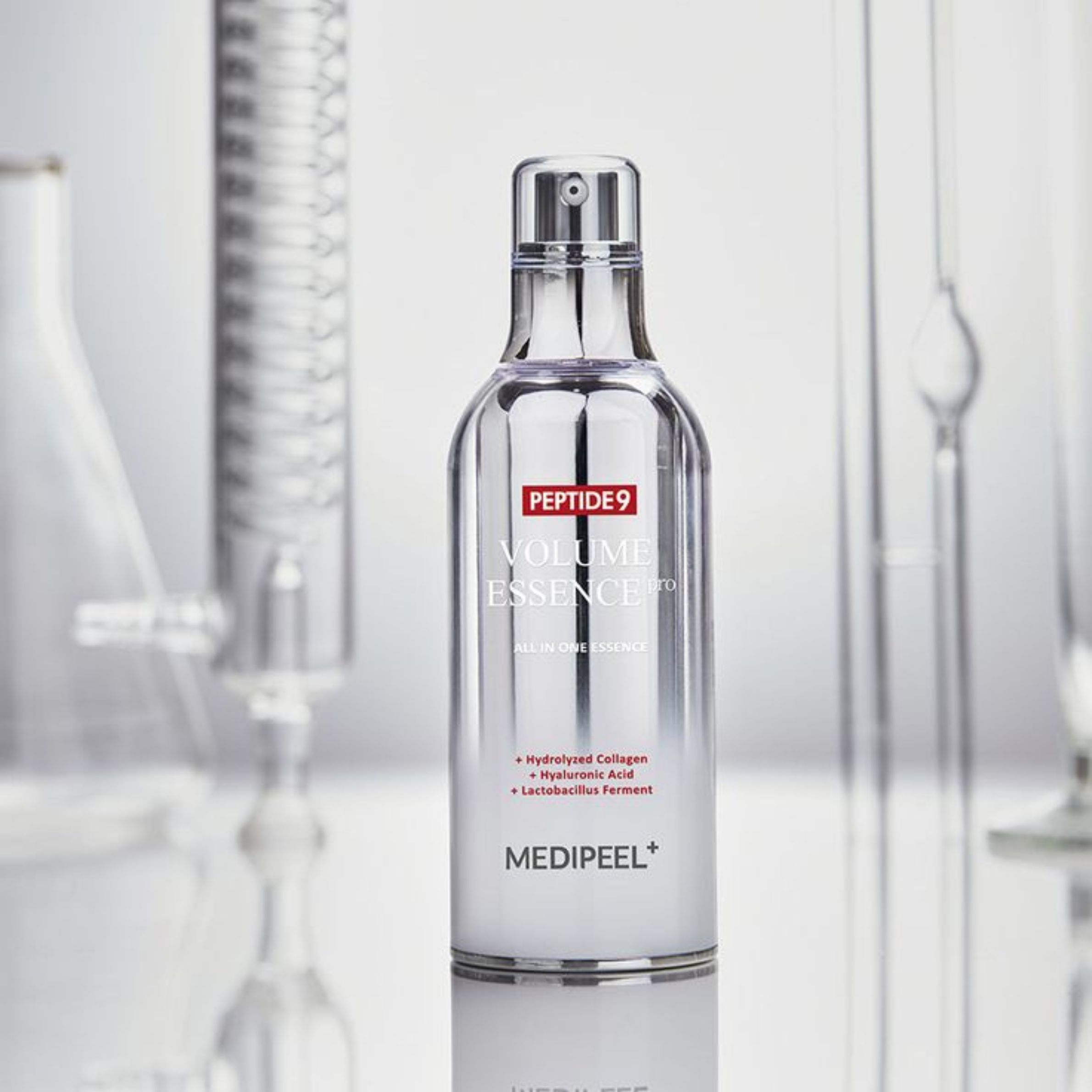 Medi-Peel Peptide 9 Volume Essence in flacone argentato, circondato da attrezzature di laboratorio. Contiene collagene idrolizzato, acido ialuronico.