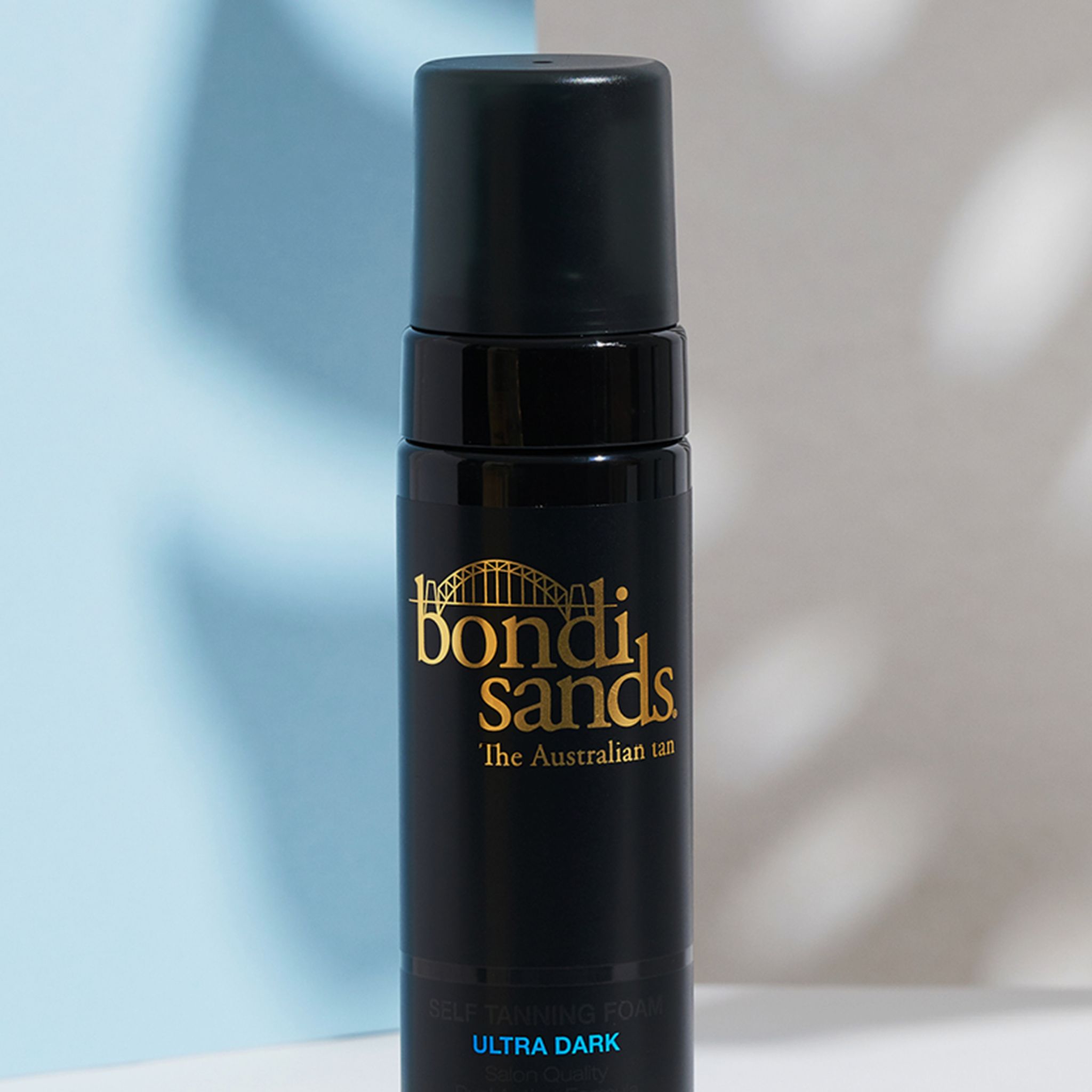 Primo piano di un flacone nero con logo dorato e erogatore nero. Scritta: Bondi Sands, schiuma autoabbronzante Ultra Dark.