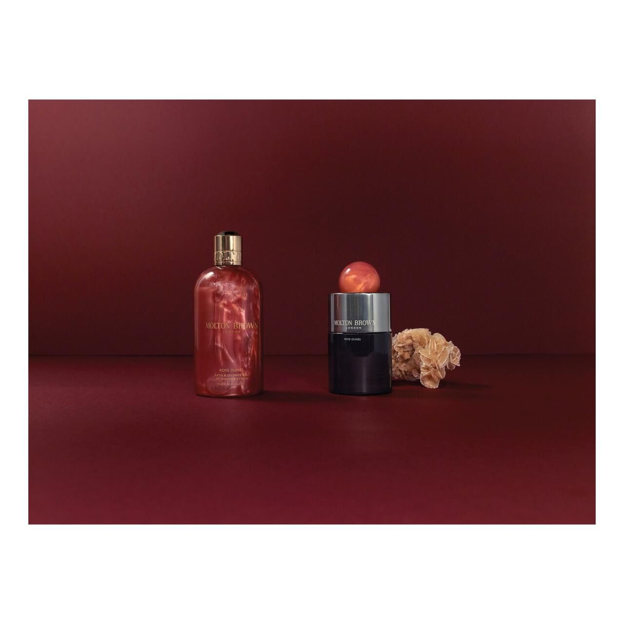 Due flaconi su sfondo rosso. Un flacone trasparente con liquido rosso, un flacone nero con coperchio.