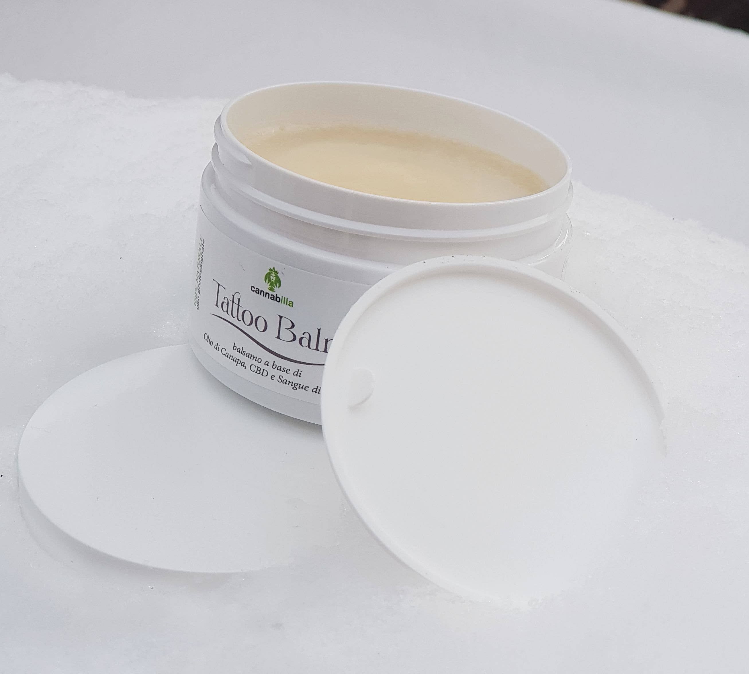Vasetto bianco con coperchio aperto. Scritta "Tattoo balm". Scritta "balsamo a base di Olio di Canapa, CBD e Sangue di Drago".