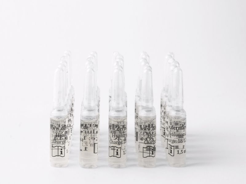 Diverse fiale di vetro con siero all'acido ialuronico, tappo bianco, etichettatura bianca.