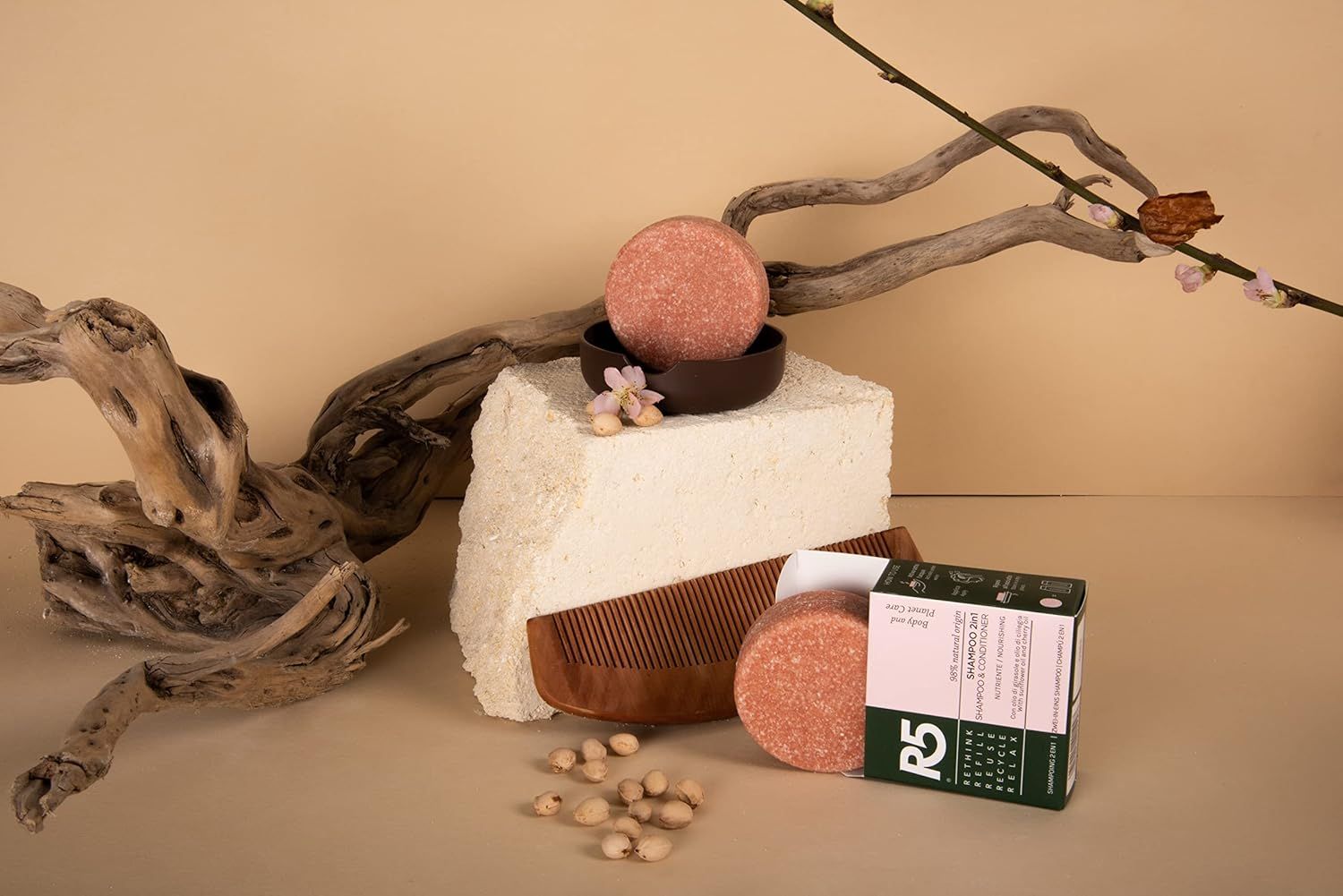 Shampoo solido rotondo rosa su un piedistallo. Accessori: pettine, confezione. Testo sulla confezione. Logo R5.