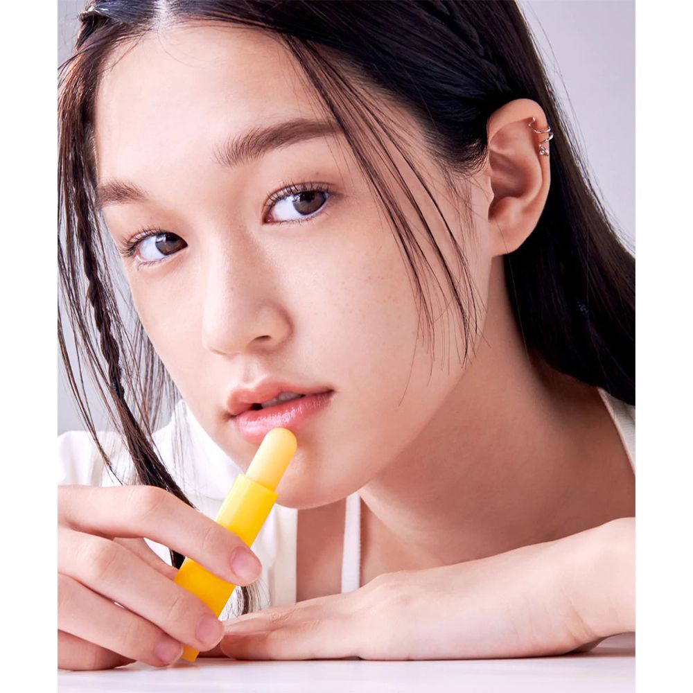 Persona che tiene un balsamo per le labbra giallo. Primo piano del viso, che guarda la fotocamera. Il balsamo viene applicato sulle labbra.
