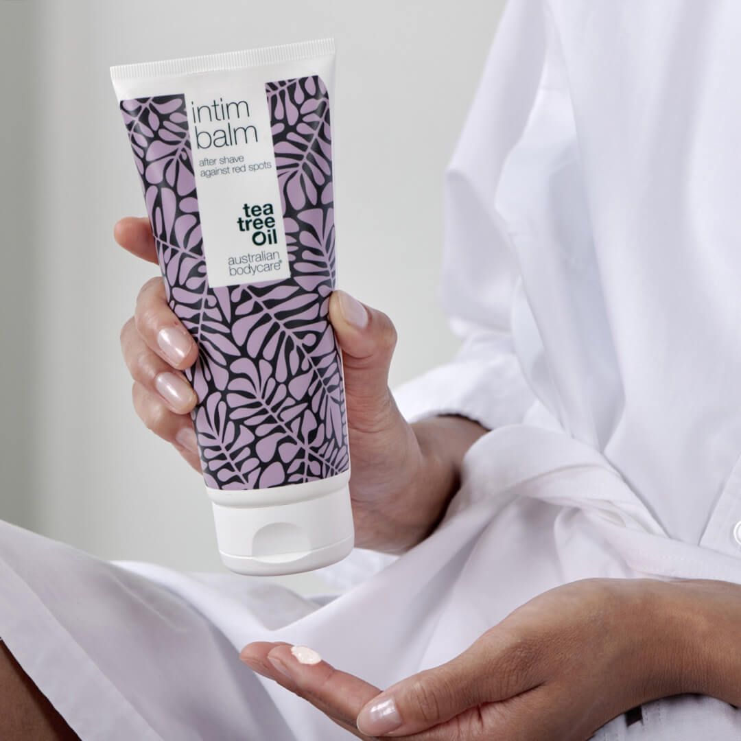 Persona che tiene un tubo di balsamo intimo. Design bianco-viola, motivo a foglie. Marchio: Australian Bodycare.