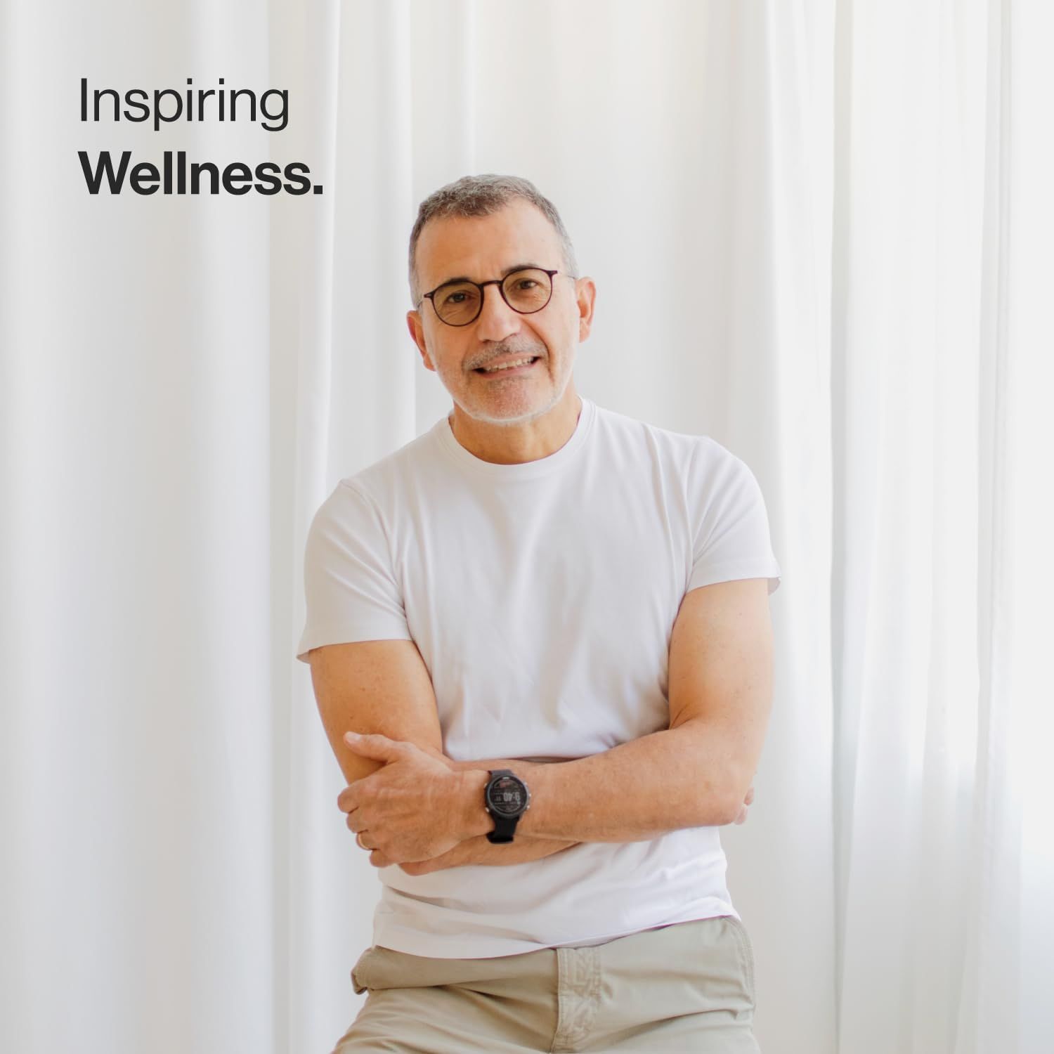 Uomo con occhiali e orologio. Sfondo: tenda bianca. Testo: Inspiring Wellness.