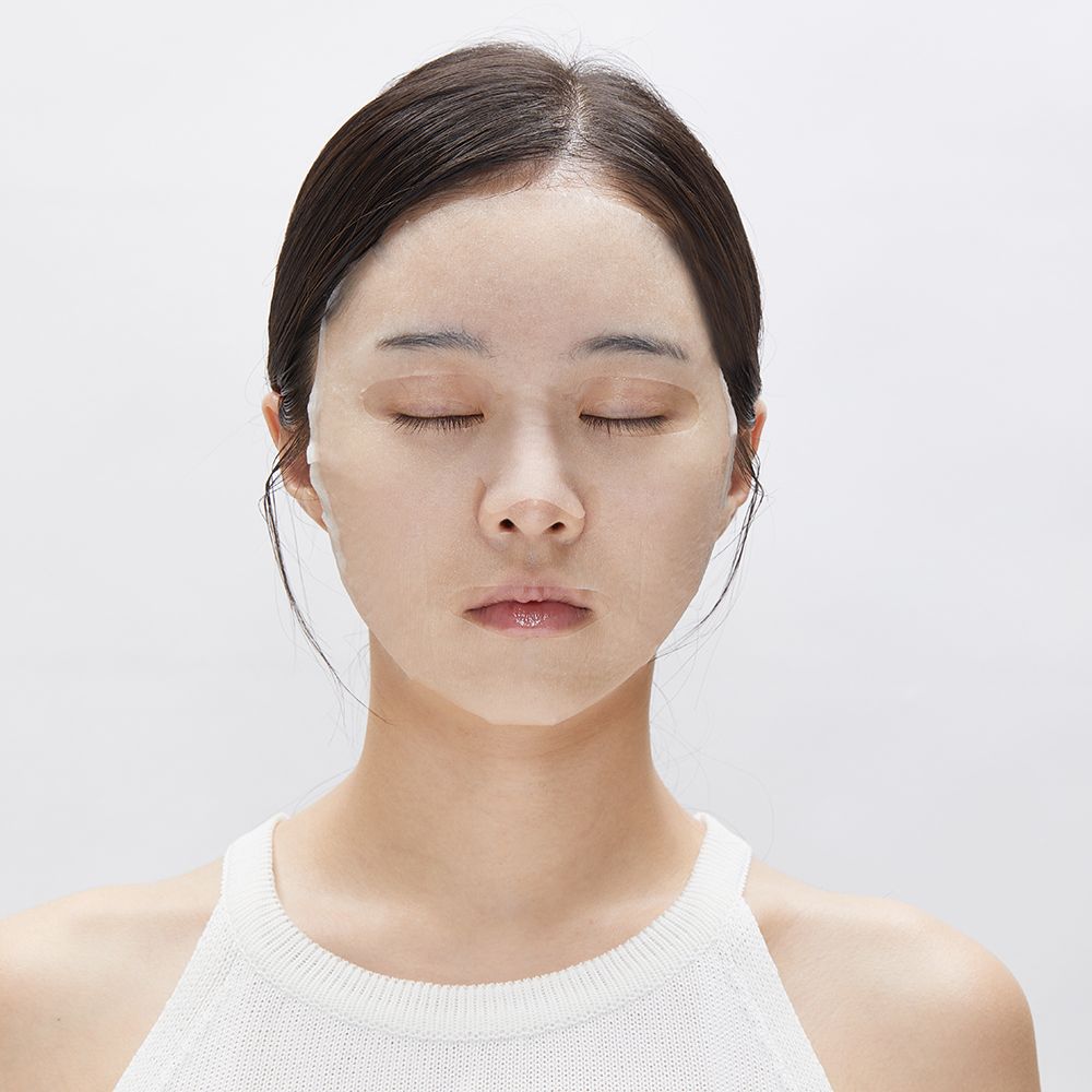 Primo piano di una donna con gli occhi chiusi che indossa una maschera per il viso. Su sfondo bianco.