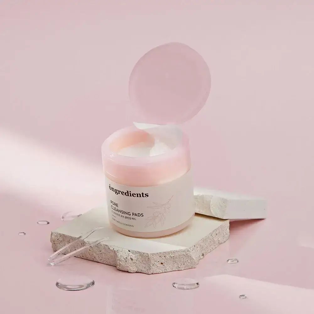 Contenitore di Pore Cleansing Pads con coperchio rosa. Etichetta bianca con testo. Posizionato su pietra, con pipetta trasparente.