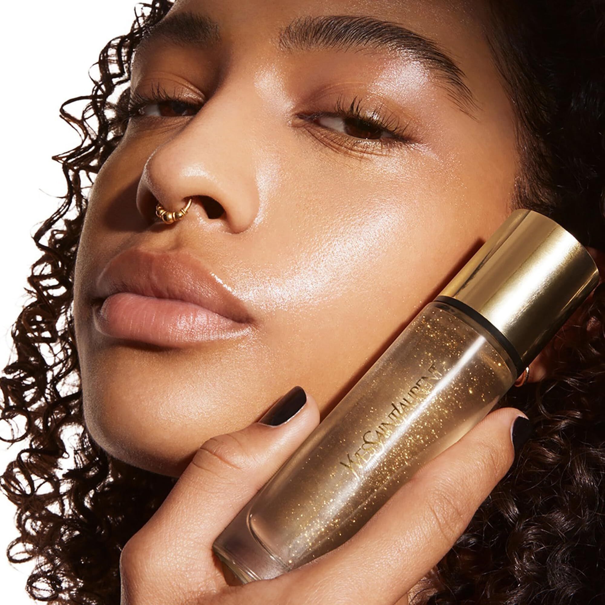 Prodotto tenuto in mano. Flacone dorato con scritta Yves Saint Laurent. Persona con piercing.