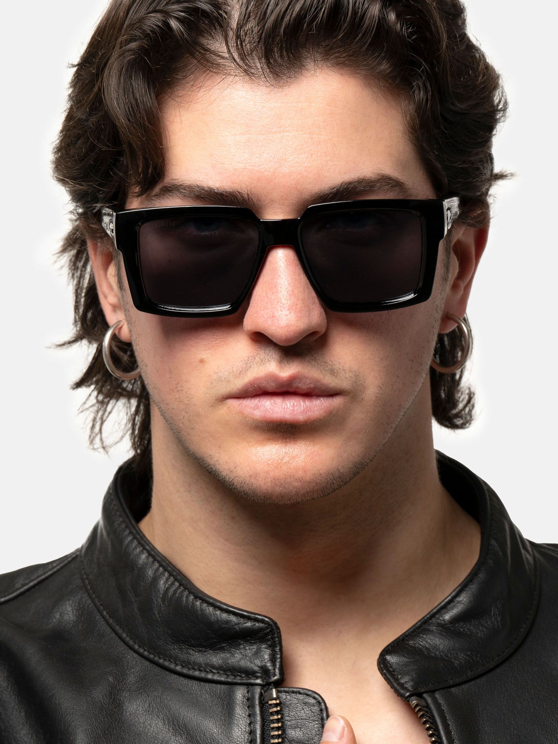 Uomo con occhiali da sole neri. Lenti rettangolari, montatura ampia. Logo Latenzazero sull'asta.