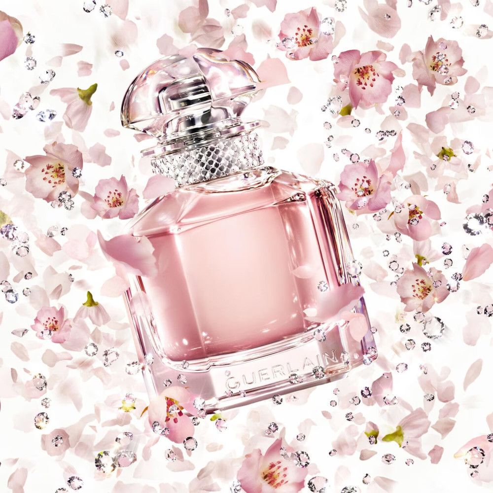 Flacone di profumo rosa con tappo trasparente e strass. Circondato da petali e cristalli. Logo Guerlain.