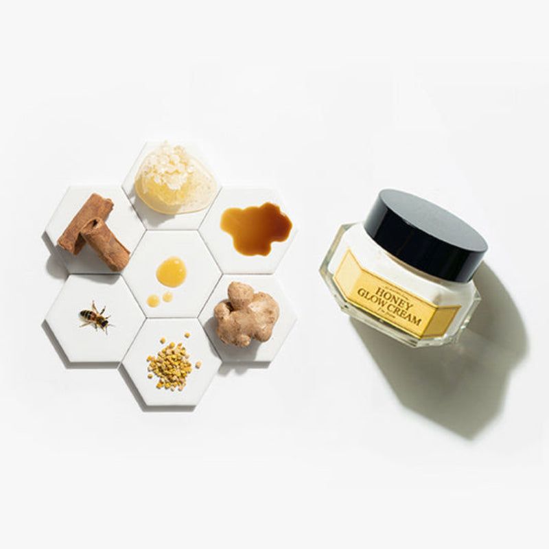 Vasetto di crema e ingredienti su piastrelle esagonali. Scritta: HONEY GLOW CREAM, I'm from. Miele, zenzero, ecc.
