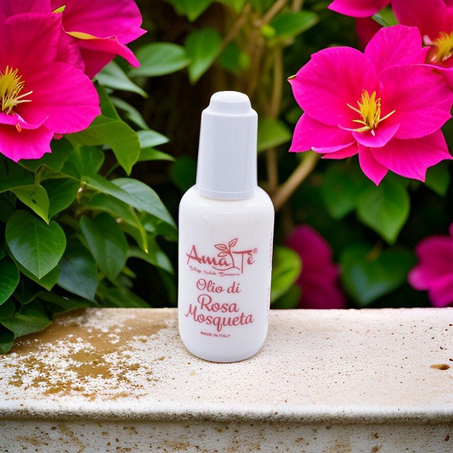 Flacone bianco con scritta rossa: Amatè Olio di Rosa Mosqueta. Made in Italy. Davanti a piante fiorite.