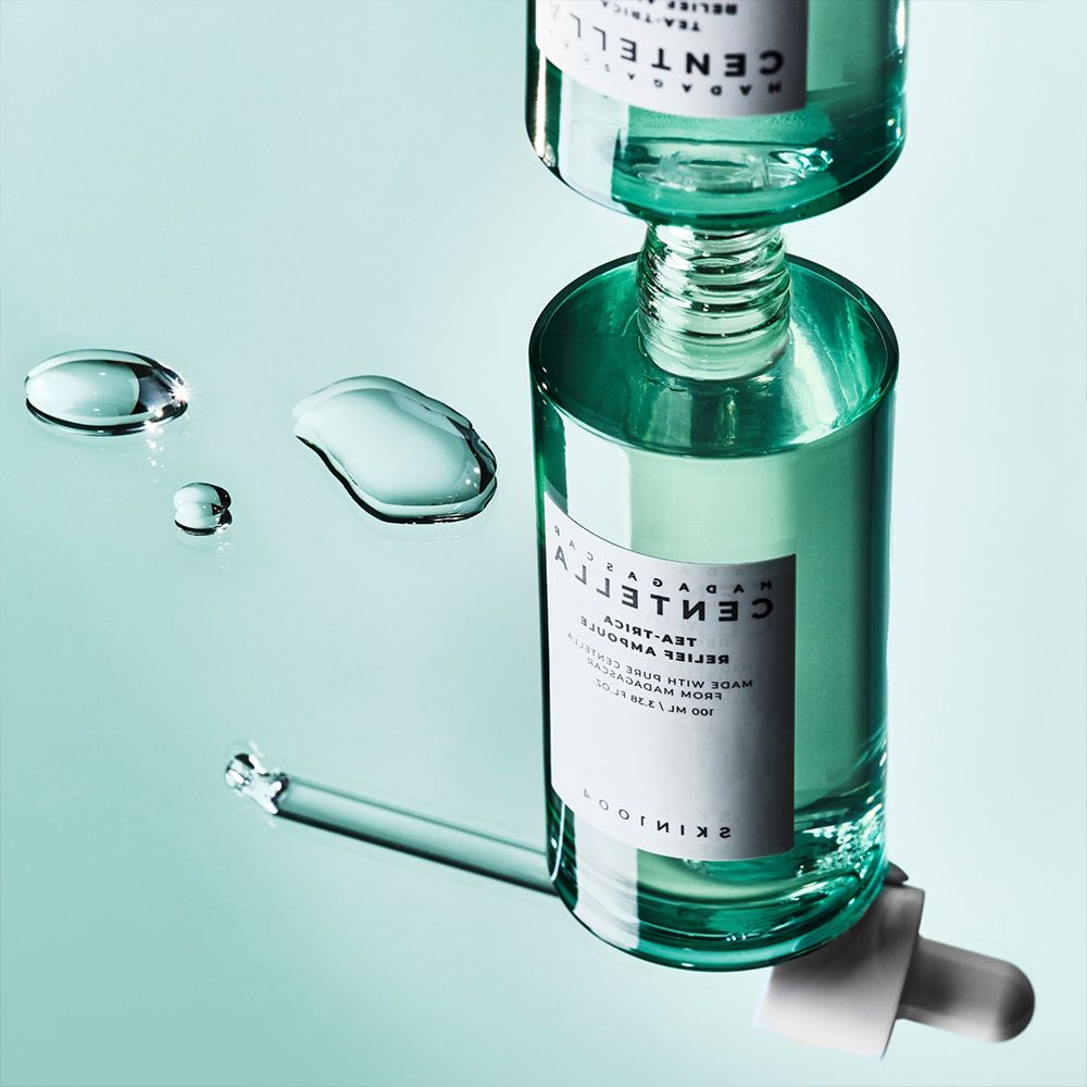 Due flaconi in vetro verde con contagocce, circondati da gocce d'acqua su una superficie riflettente.