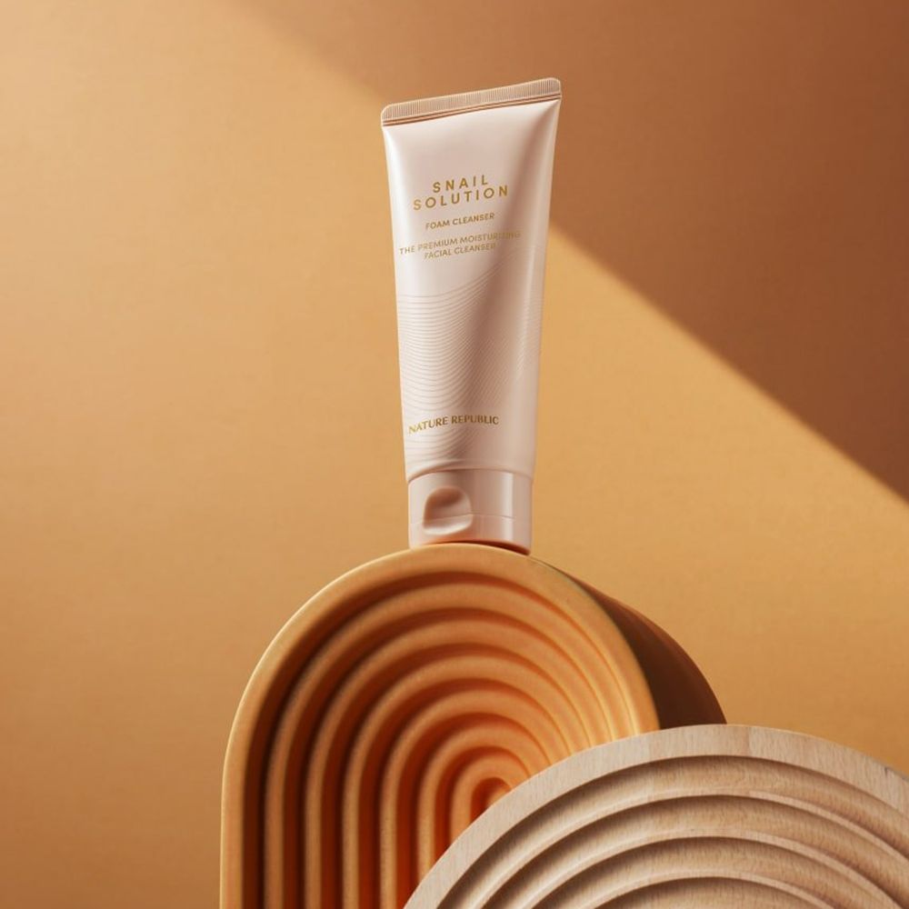 Tubo beige su struttura in legno. Testo del prodotto: Snail Solution Foam Cleanser.