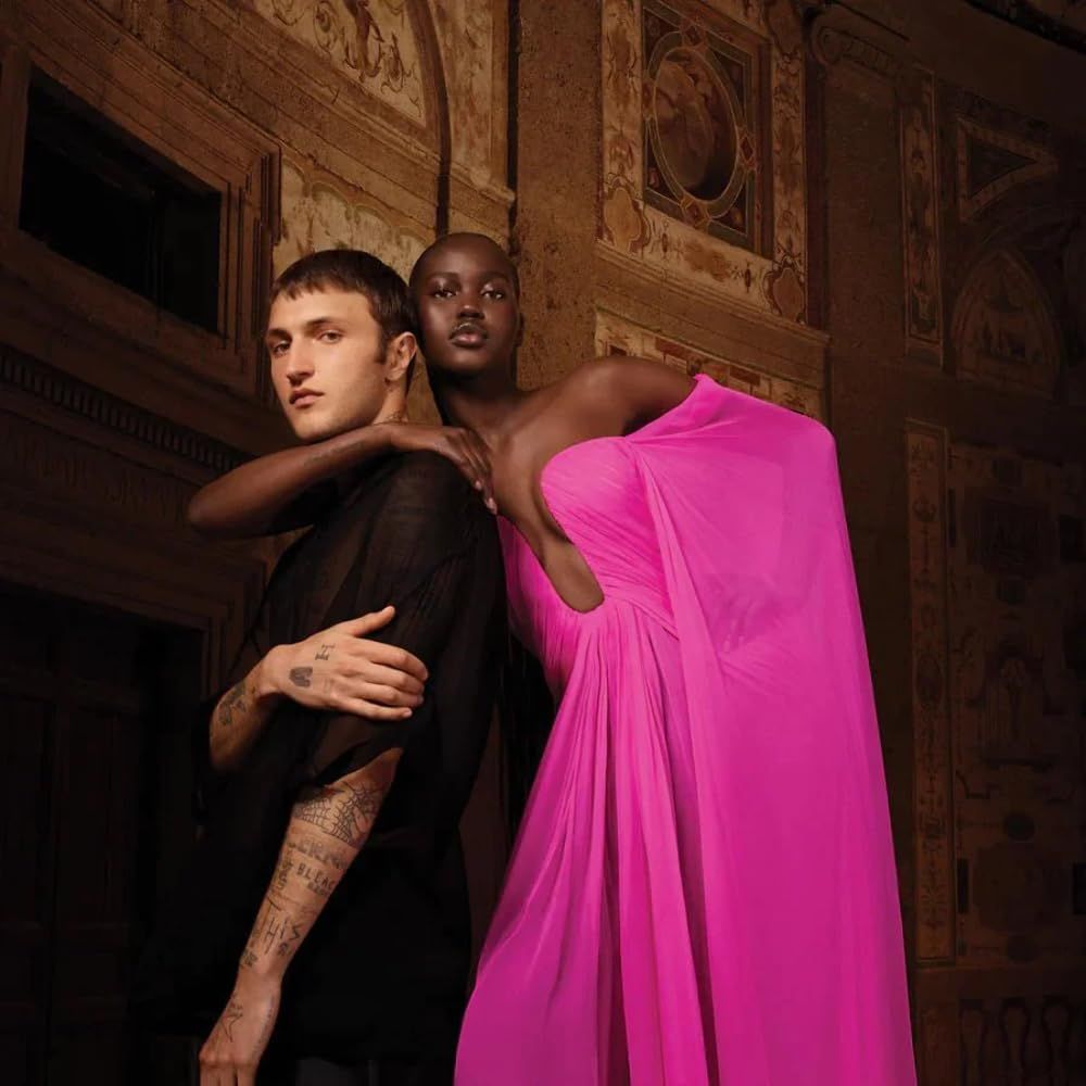 Due persone davanti a un affresco. Una persona in nero, l'altra in un abito rosa. Entrambi guardano la fotocamera.