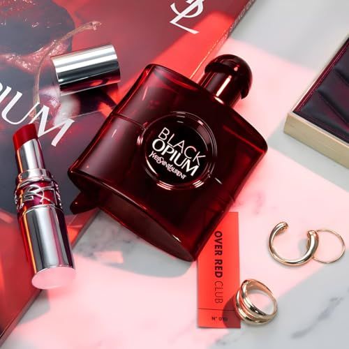 Flacone rosso, rossetto, gioielli e confezione su una superficie.