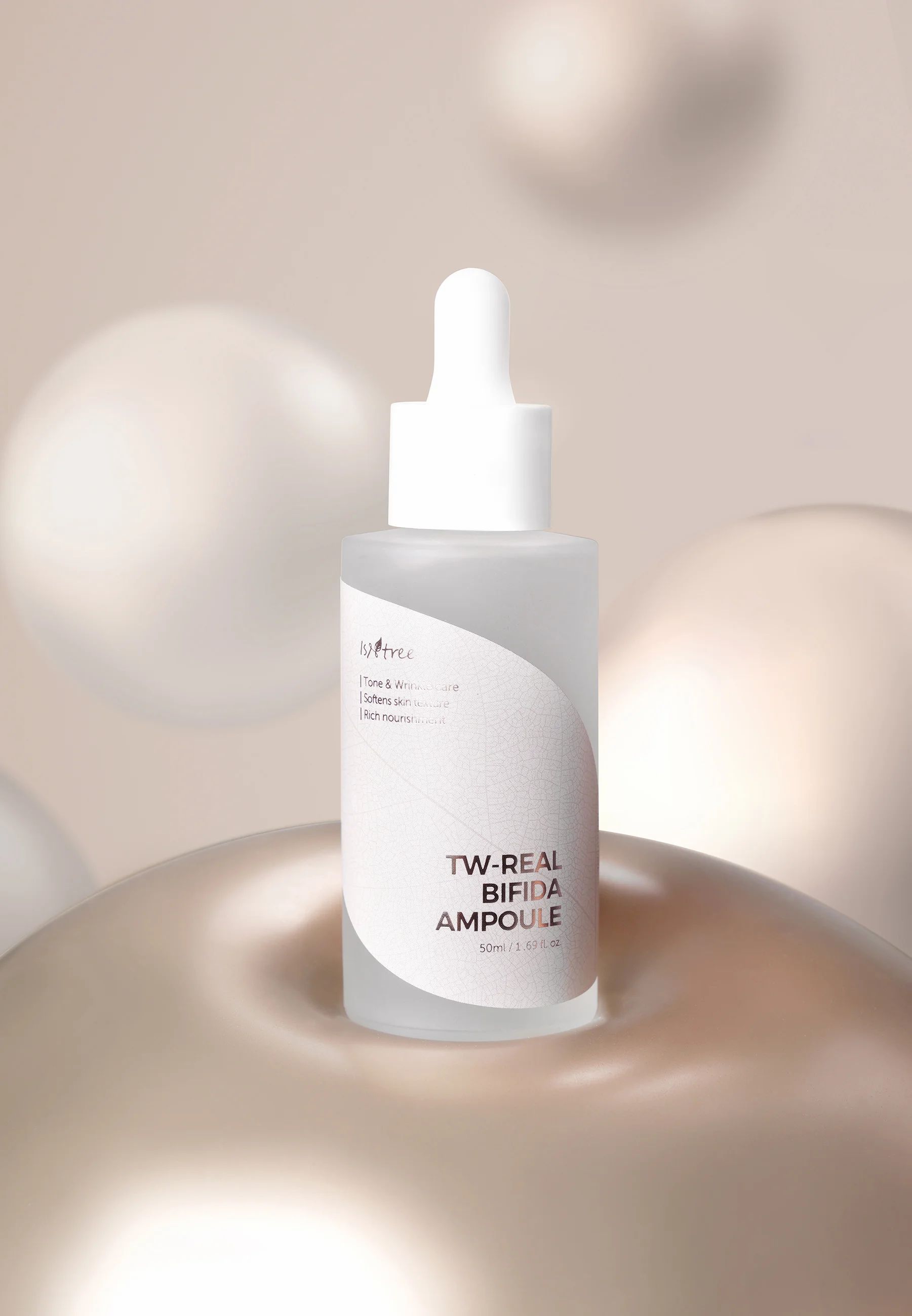 Flacone in vetro con tappo bianco, scritta TW-REAL BIFIDA AMPOULE. Su piedistallo dorato, circondato da sfere.