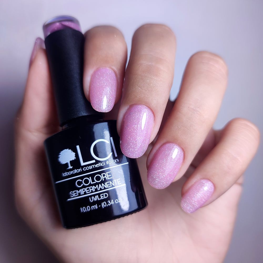 Mano con unghie smaltate e flacone di smalto. Smalto semipermanente rosa. Scritta: LCI, Colore Semipermanente.