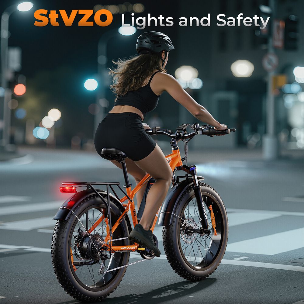 Persona in sella a e-MTB VARUN arancione di notte. Illuminazione StVZO. Abbigliamento nero, casco.