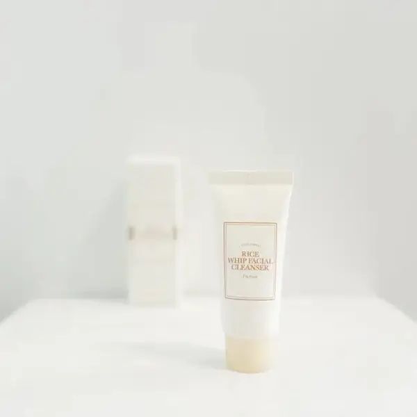 Tubo bianco con scritta "Rice Whip Facial Cleanser". Dietro, un contenitore rettangolare. Entrambi su sfondo bianco.