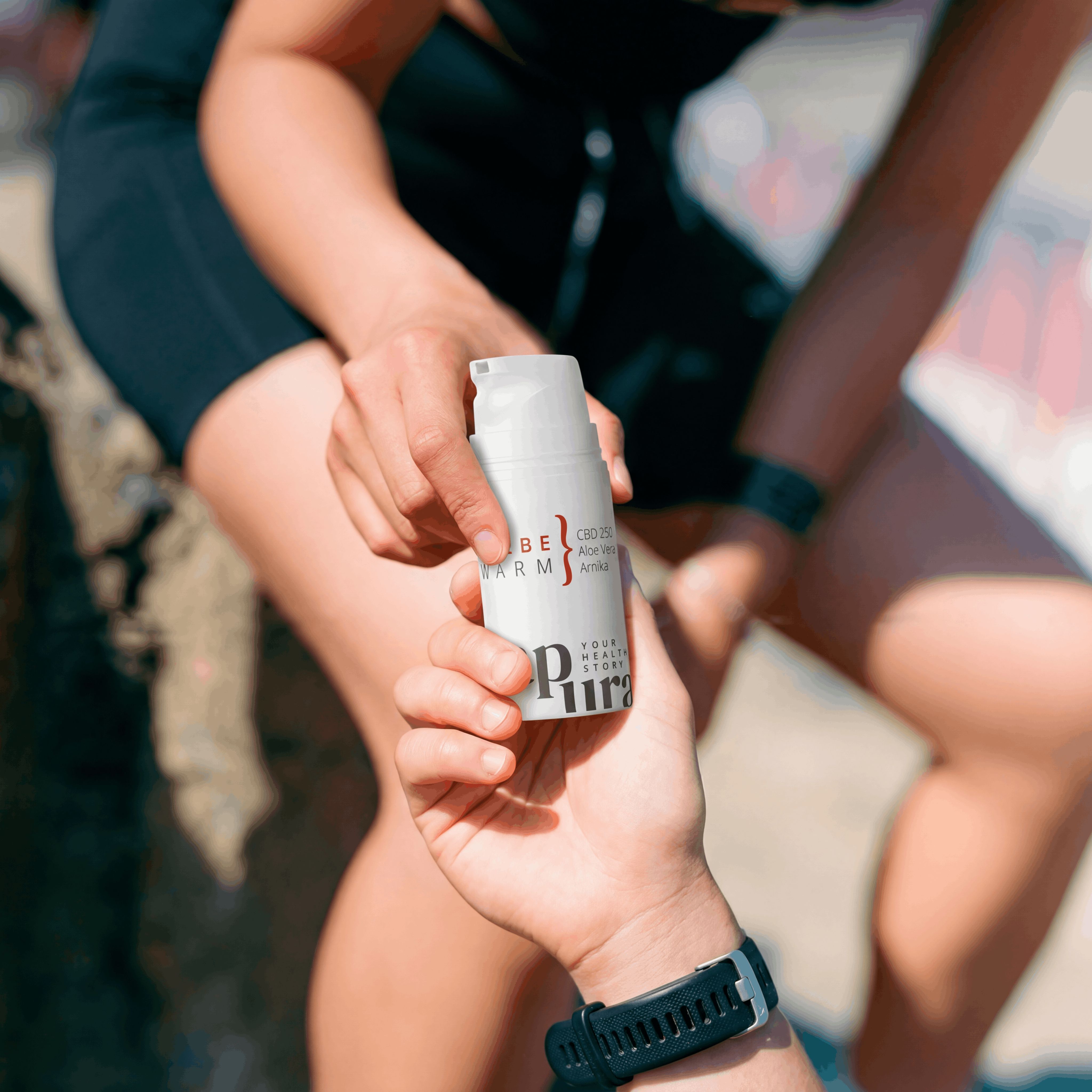 Due mani si passano un flacone a pompa bianco con scritta "CBD SALBE WARM" e "CBD 250mg Aloe Vera Arnika".