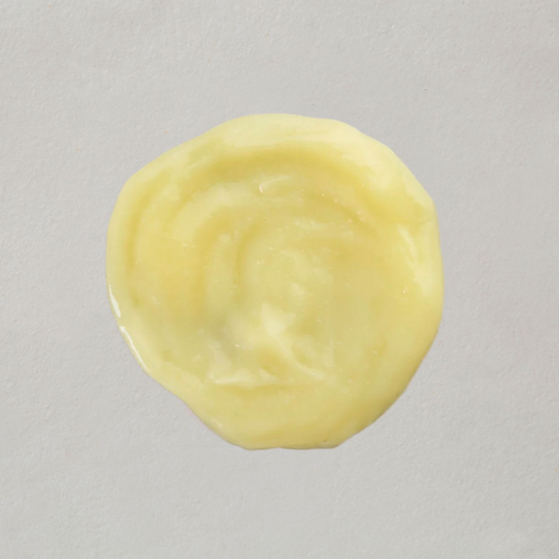 Una piccola quantità di balsamo cremoso e giallo per capelli su sfondo chiaro.