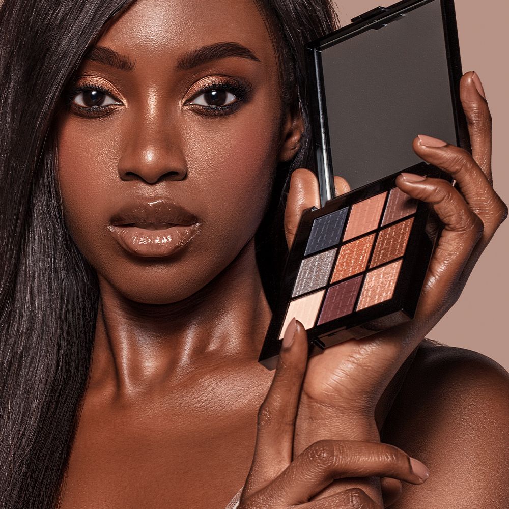 Donna di colore tiene in mano una palette ombretti aperta. Nove tonalità, cornice nera. Specchio nel coperchio.