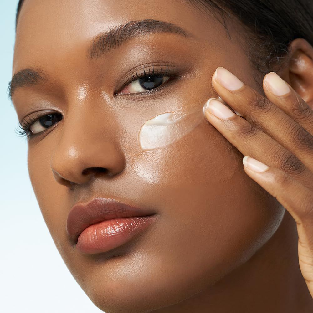 Una donna applica una crema bianca sulla guancia, primo piano.