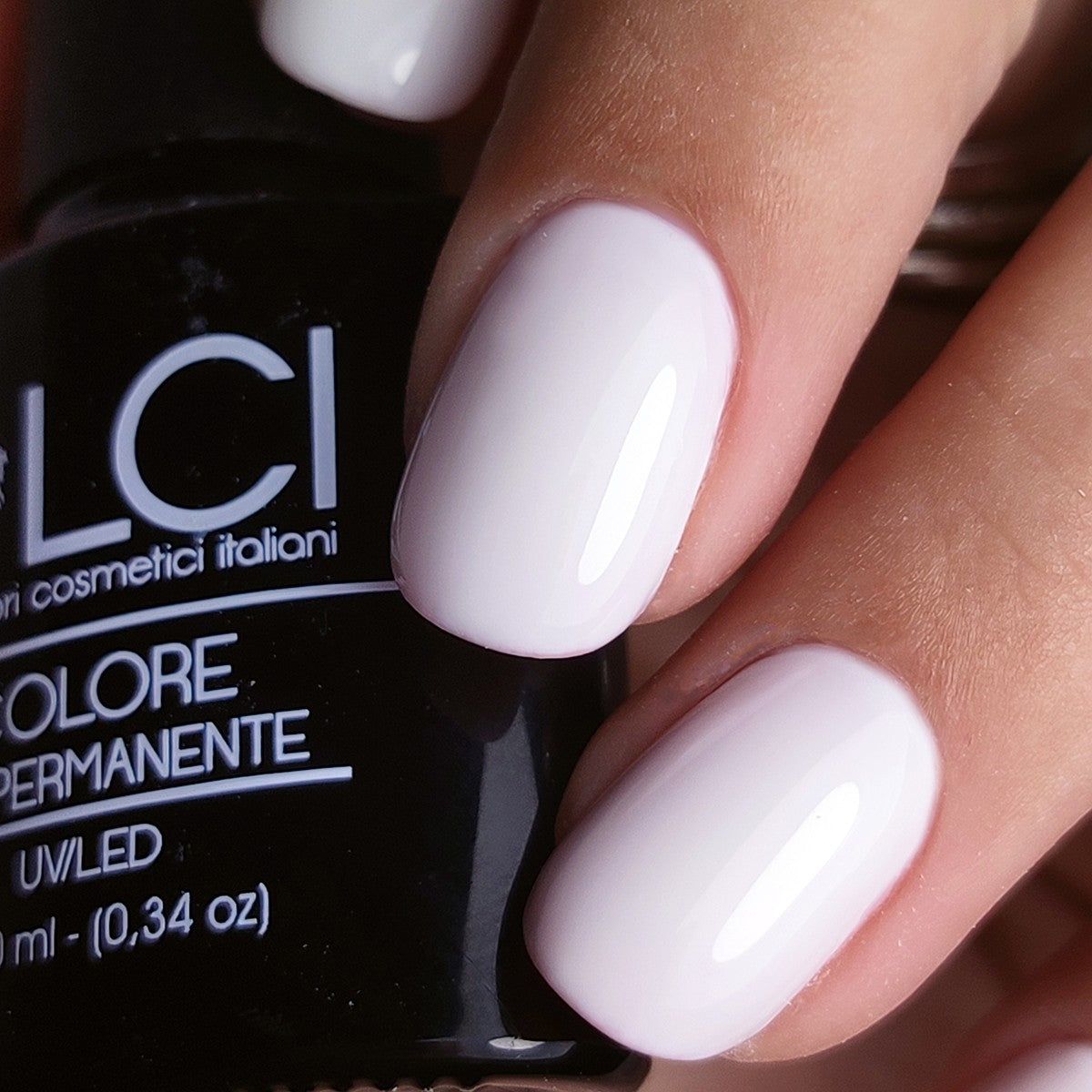 Mano con unghie smaltate. Flacone di smalto sullo sfondo. Scritta: LCI, Colore Semipermanente, UV/LED.