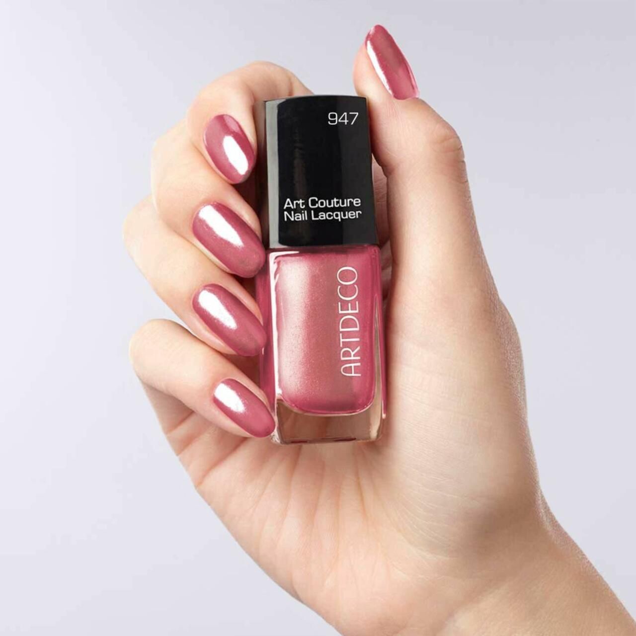 Mano che tiene un flacone di smalto per unghie e unghie smaltate. Scritta: Artdeco, Art Couture Nail Lacquer, 947.