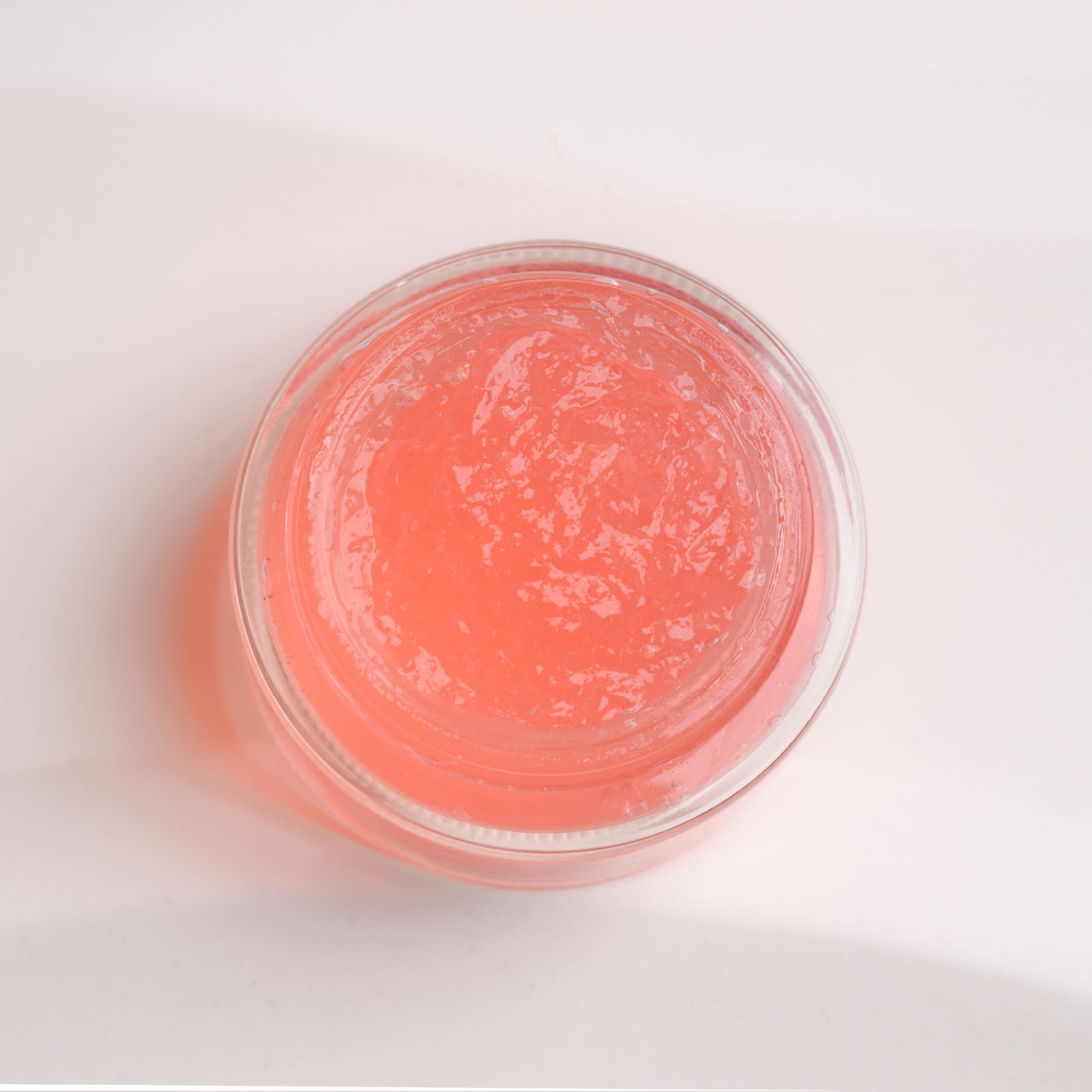 Vista dall'alto di una crema gel rosa in un contenitore di vetro trasparente. Il contenuto è visibile.