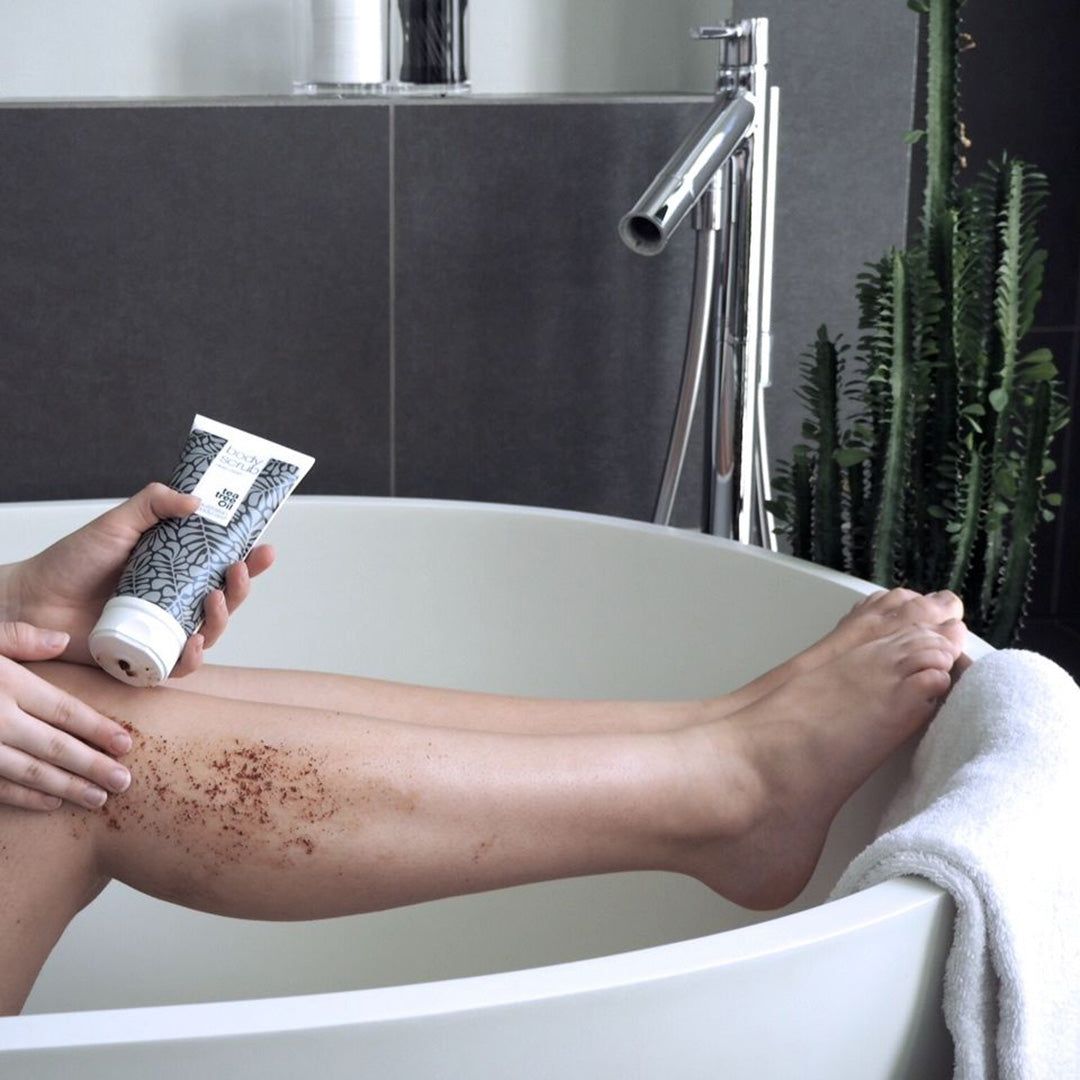 Persona in vasca da bagno. Tiene un tubetto di Body Scrub. Gamba esfoliata. Marchio: Australian Bodycare. Contesto: bagno.