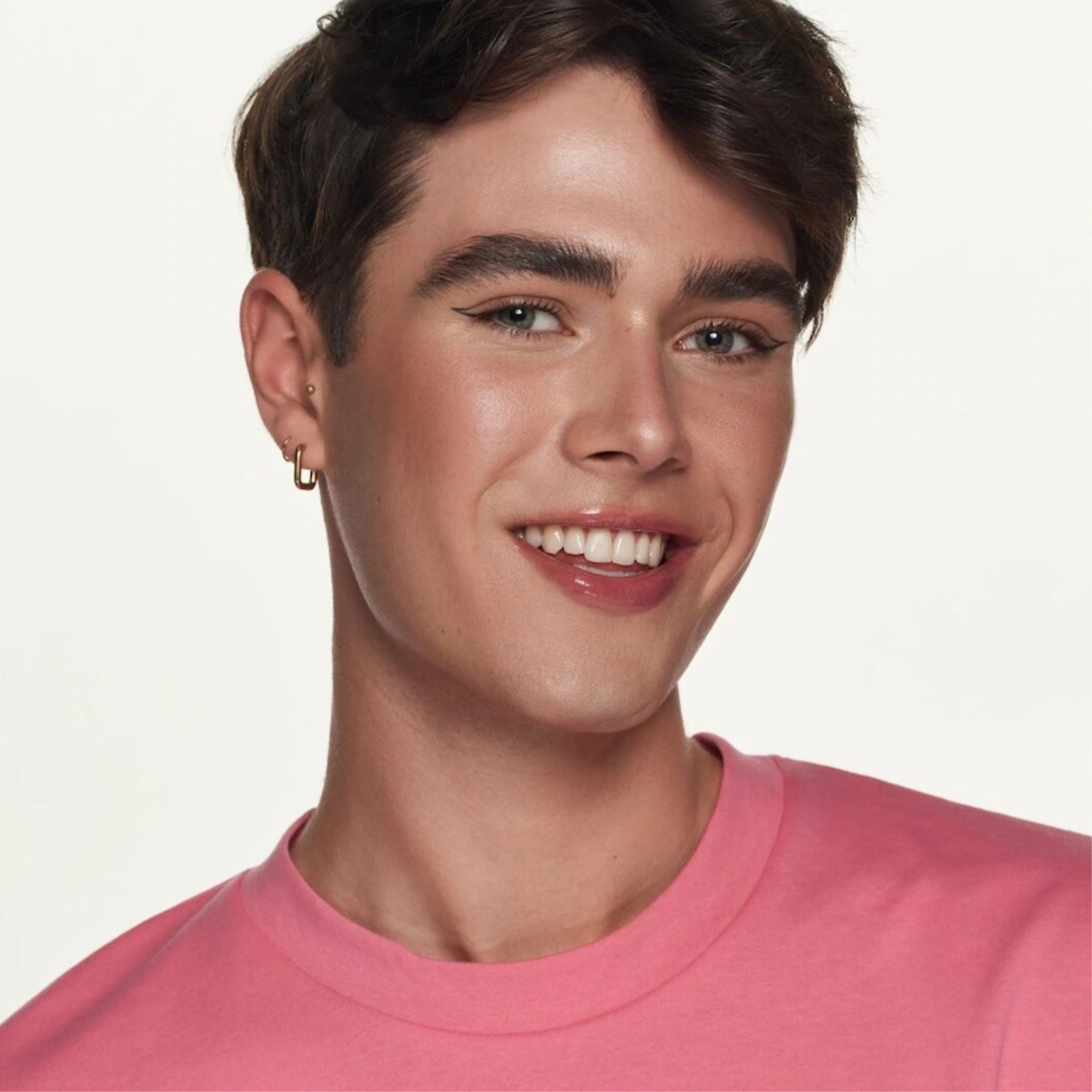 Ritratto di un uomo con labbra rosa. Indossa una maglietta rosa e ha un incarnato chiaro. Sorride.