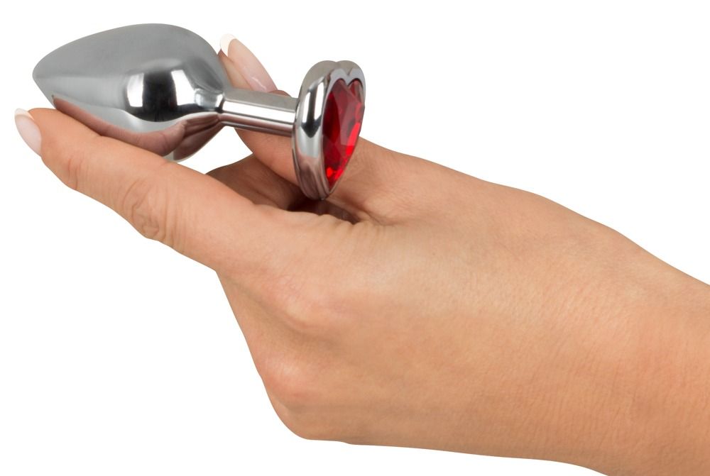 Mano che tiene un plug anale con pietra rossa a forma di cuore. Metallo argentato.