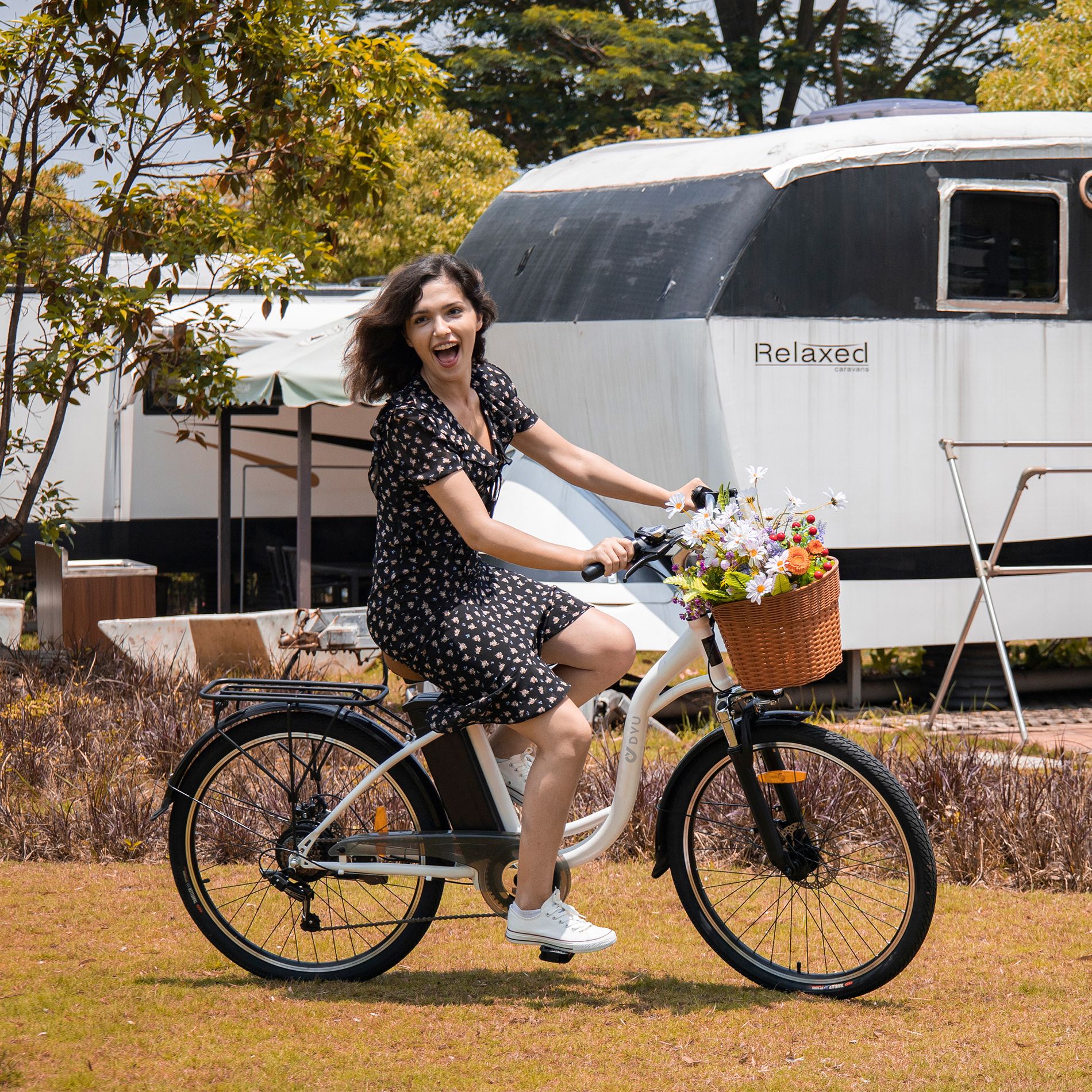 Donna su bici bianca con cestino e fiori. Telaio nero. Sfondo: edificio.