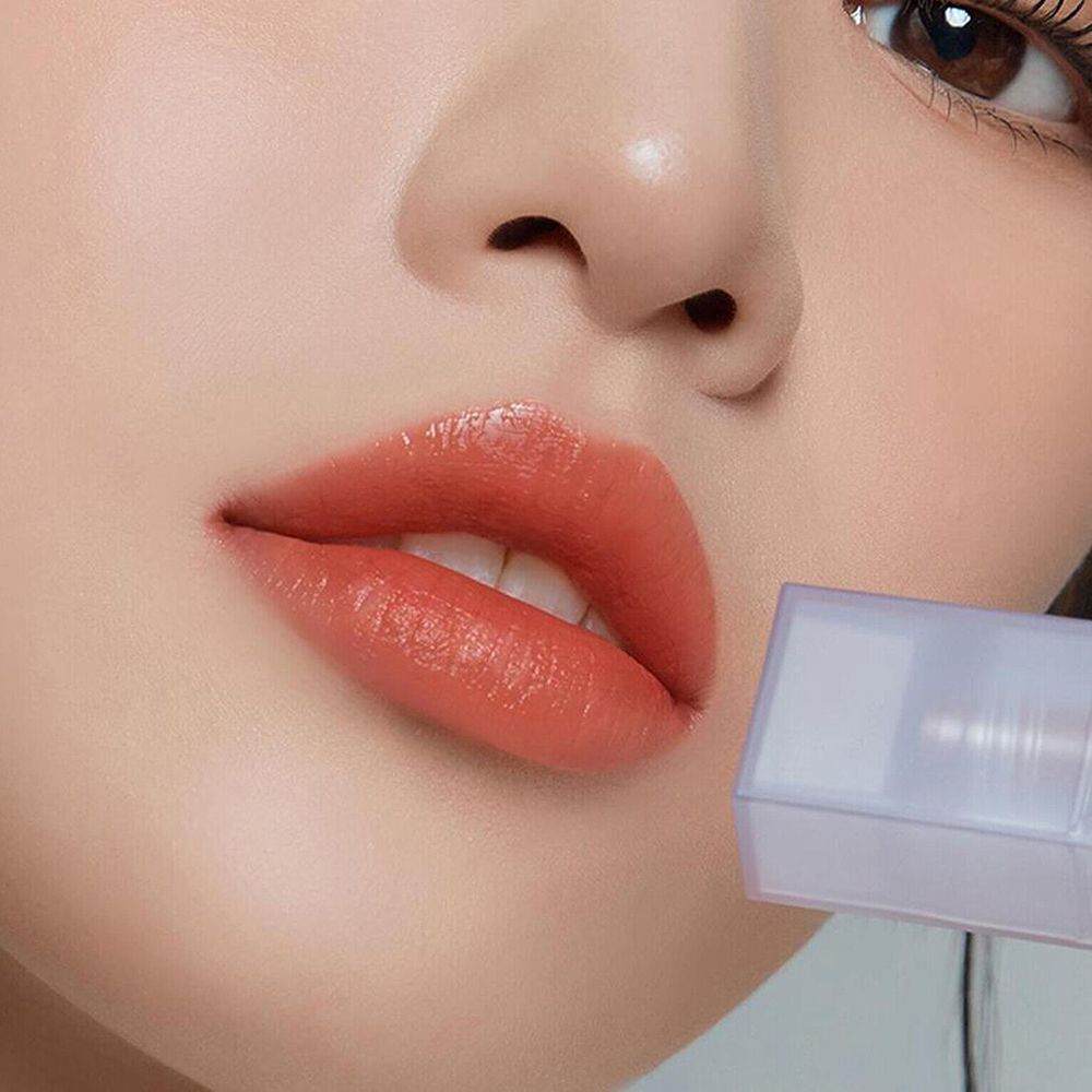 Primo piano di labbra con gloss applicato. Colore albicocca. Flacone di rossetto sullo sfondo.