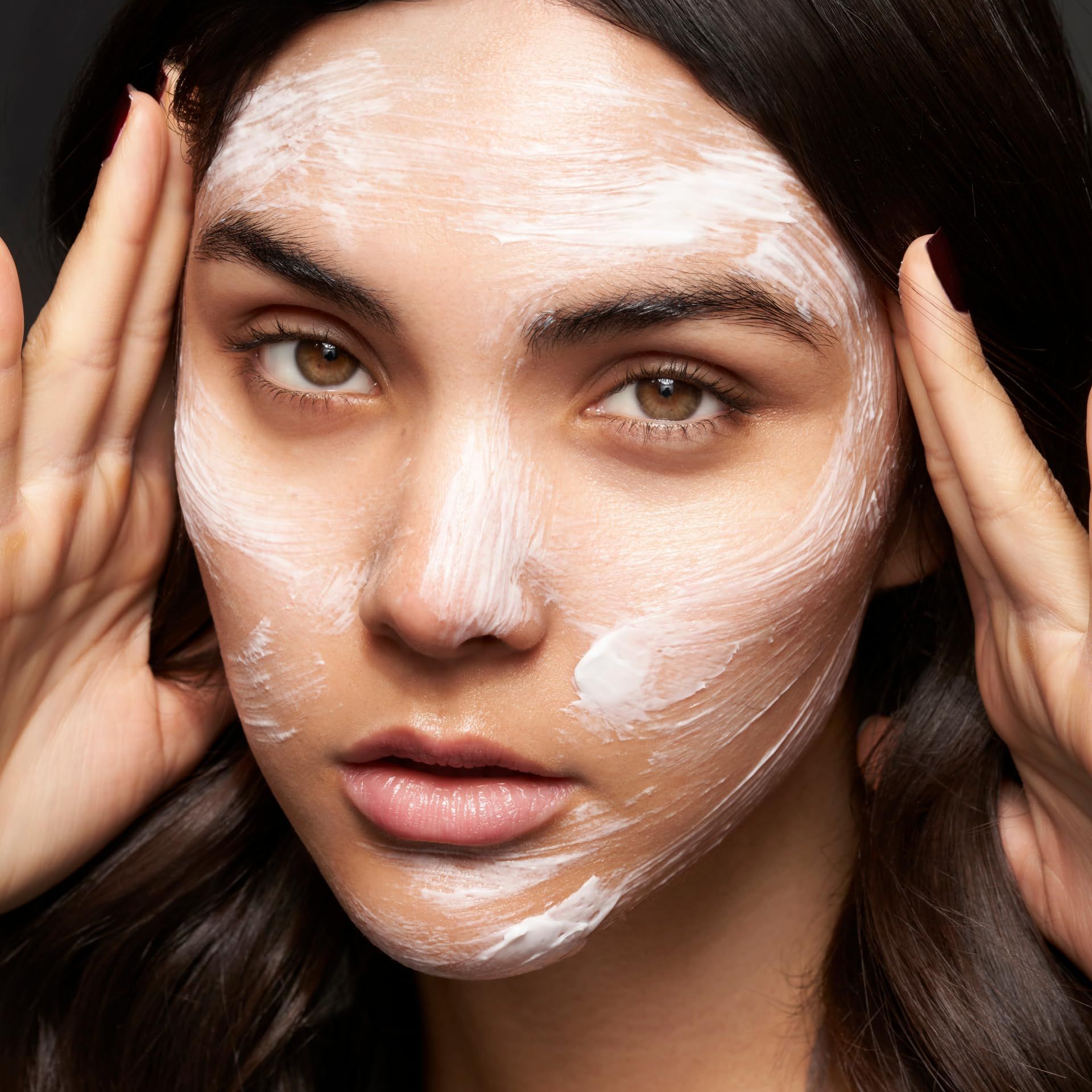 Primo piano di un viso con crema bianca. Mani che toccano il viso.
