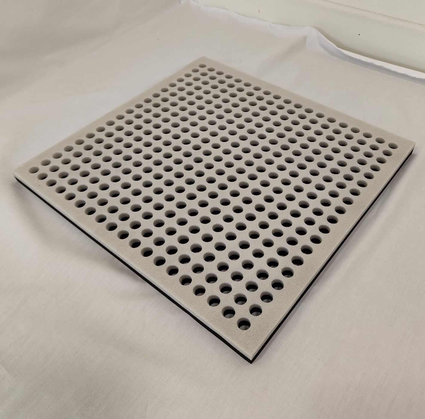 Una lastra quadrata chiara perforata. La lastra è su una superficie bianca. I fori sono distribuiti uniformemente.