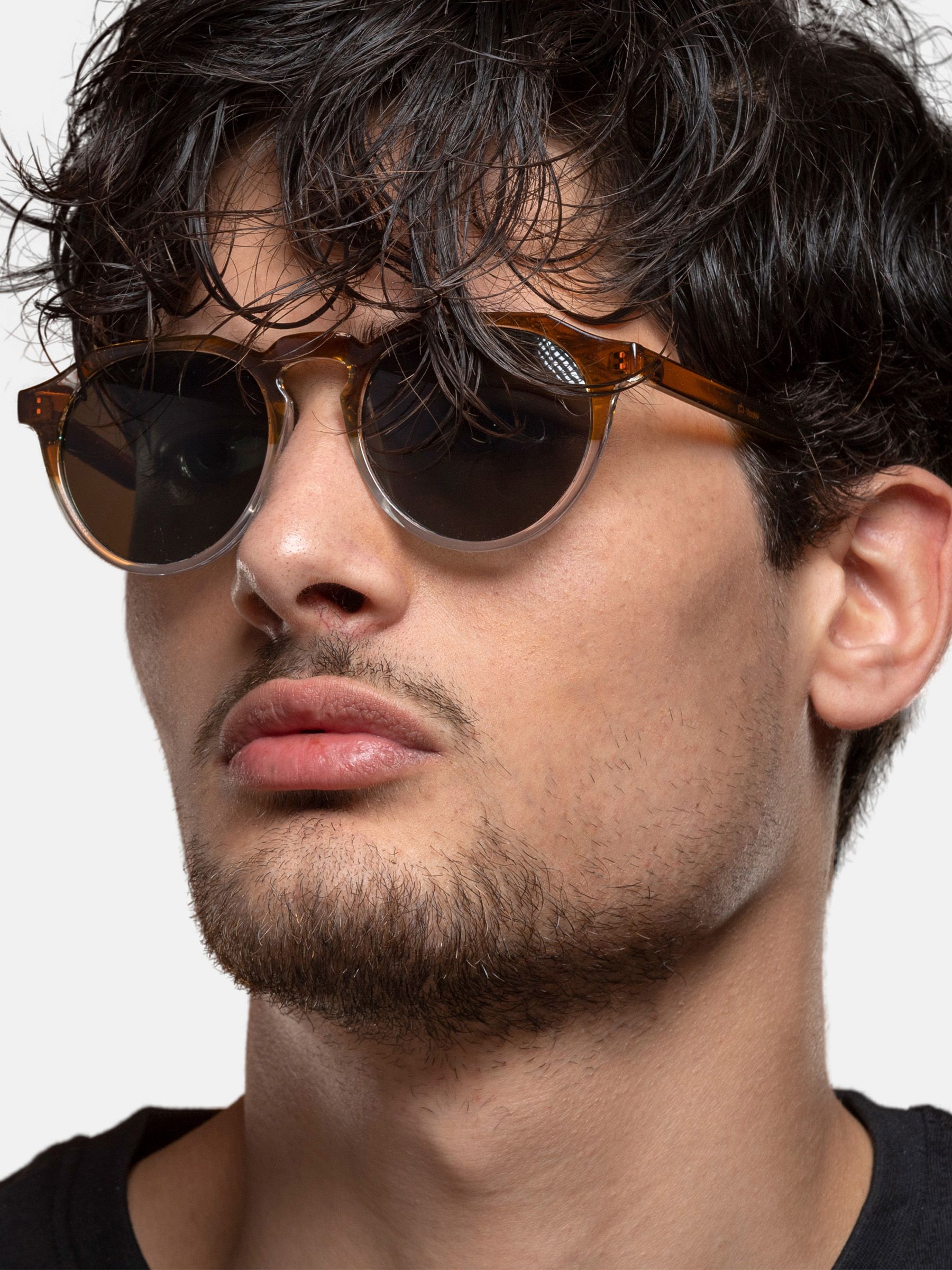 Uomo con occhiali da sole con montatura marrone e lenti rotonde. Parte inferiore delle lenti trasparente.