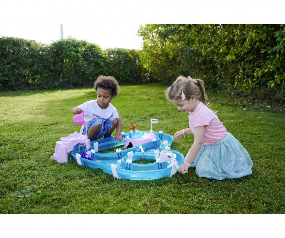 Due bambini giocano con un gioco d'acqua blu e rosa in giardino. Un bambino versa acqua con un bicchiere rosa.